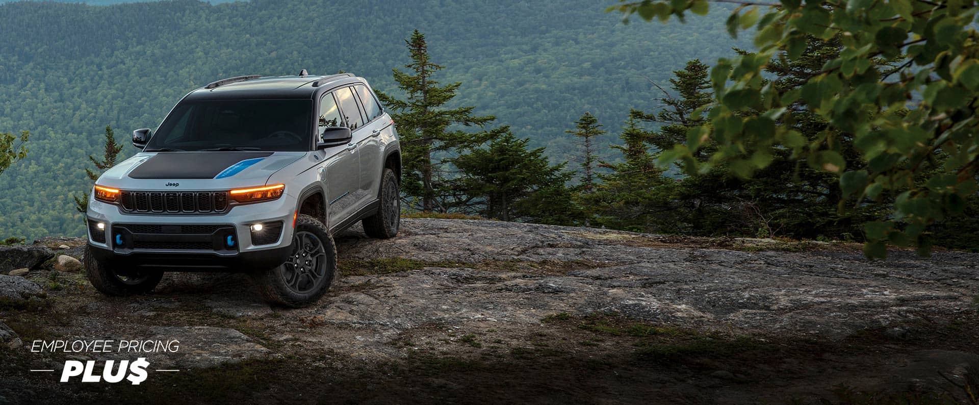 Un Jeep Grand Cherokee Trailhawk 2024 plateado con inserción negra en el capó, estacionado en el borde de un precipicio, en las montañas. Precios de empleado.