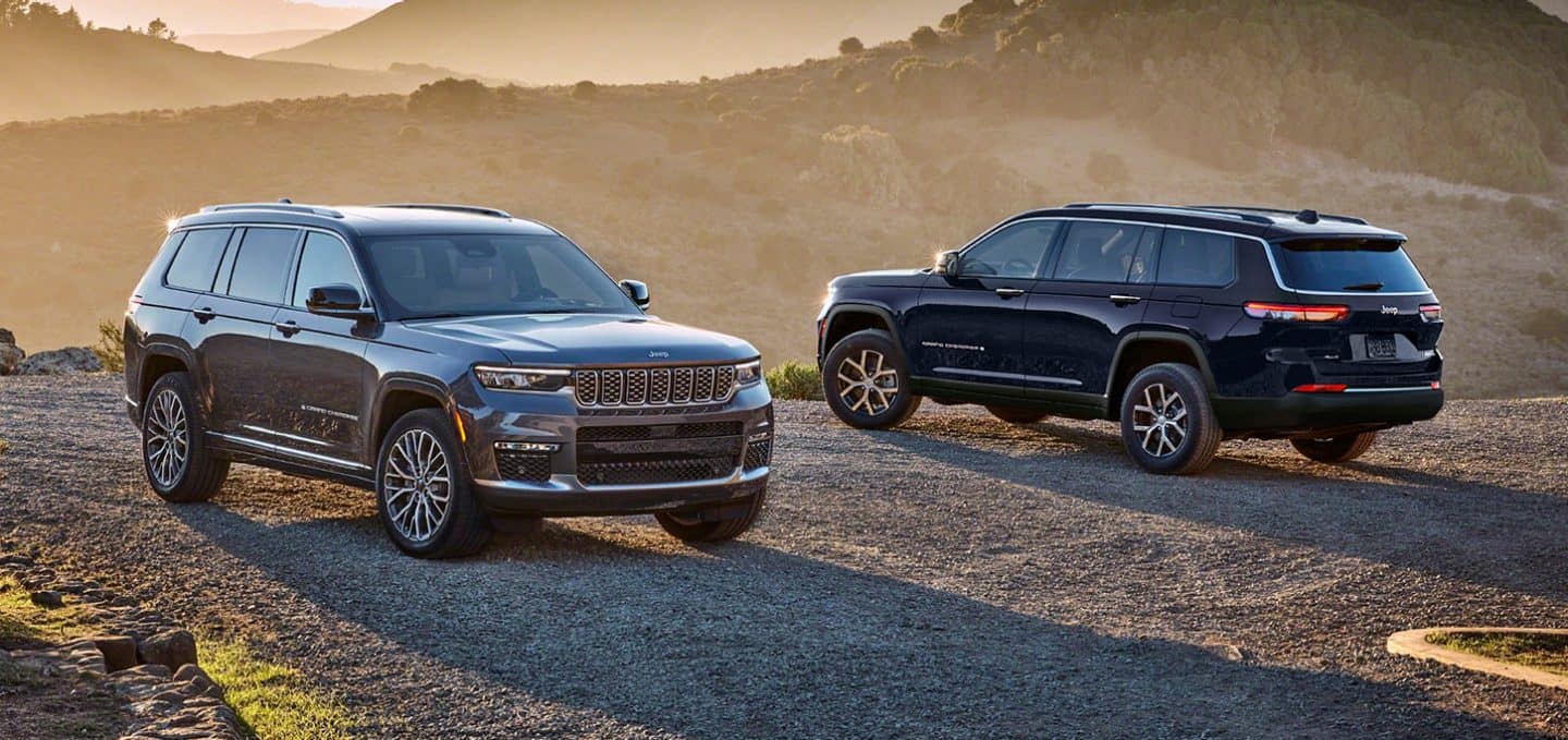 Display A gray 2025 Jeep Grand Cherokee Summit Reserve and a blue Jeep Grand Cherokee Limited parked opposite of each other on a gravel mountain road at sunset. 